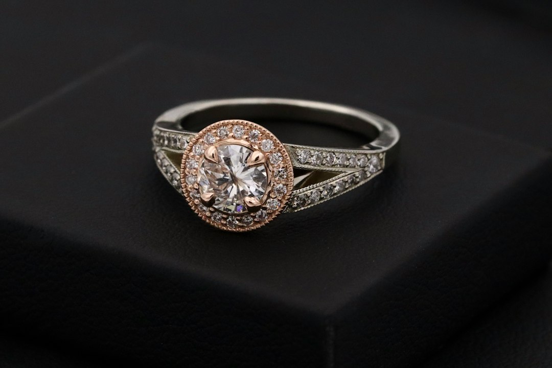 Two-tone diamond engagement ring with round brilliant cut diamond in the center of rose gold halo and white gold split shank set with diamonds.